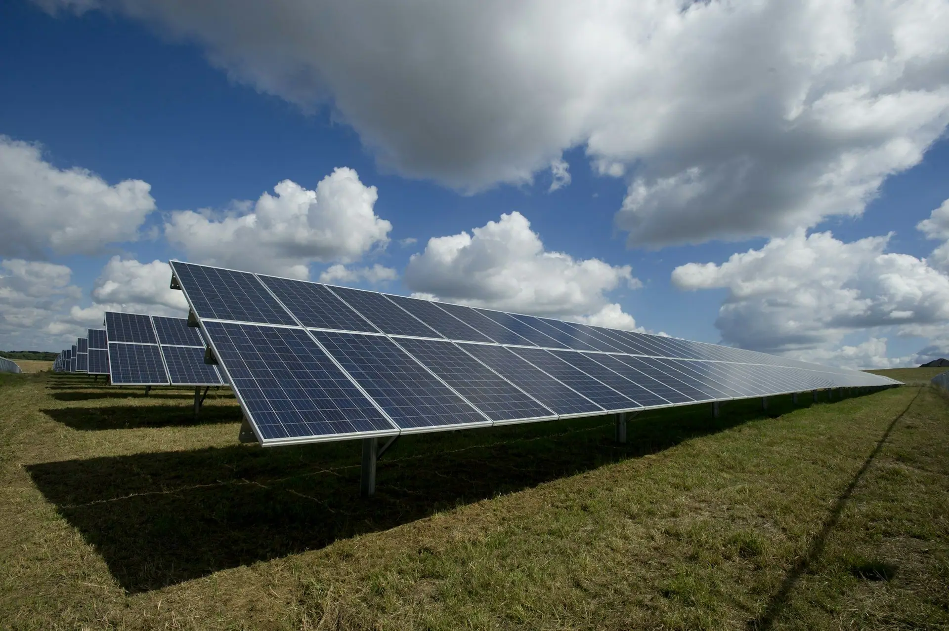 Ground-mounted solar panels on a green field under a bright sky