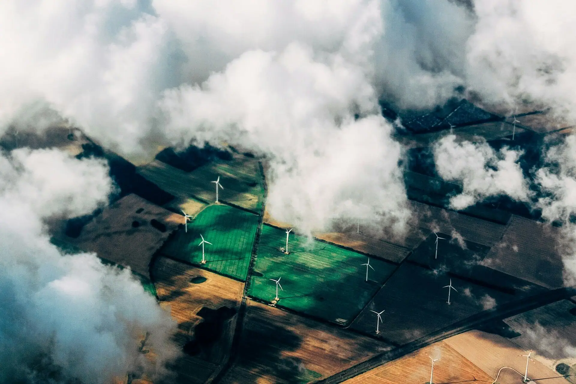 Aerial view of wind turbines across farmland seen through clouds